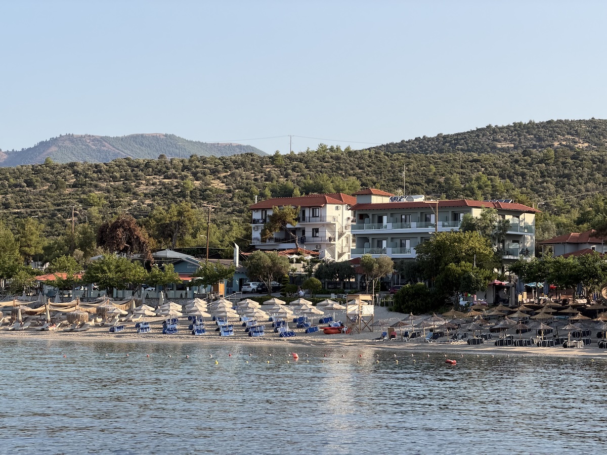 Blick auf den Strand von Pefkari auf Thassos mit blauem Meer, Sonnenschirmen, Hotel und bewaldeten Hügeln bei Potos