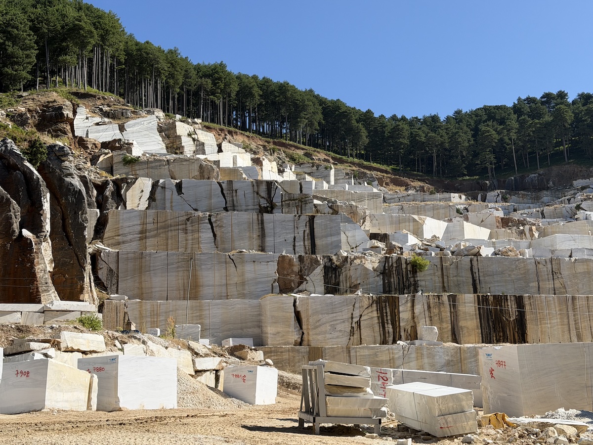 Heller Marmorsteinbruch mit gestuften Felswänden, Natursteinblöcken und dichtem Wald unter blauem Himmel auf Thassos