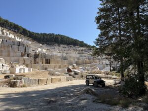 Ein Geländewagen steht zwischen bearbeiteten Marmorblöcken in einem weitläufigen Steinbruch unter blauem Himmel.
