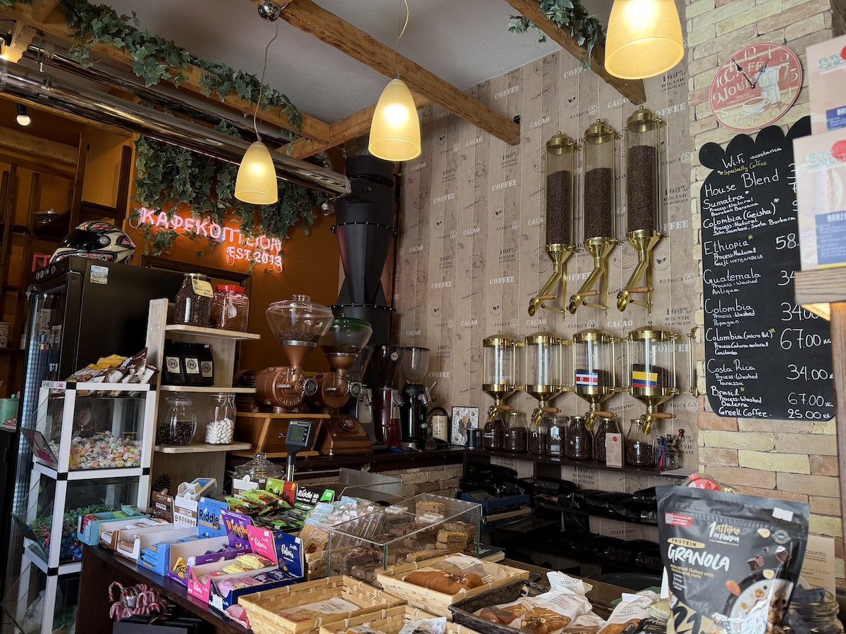Warmer Innenraum des Raw Cherry Coffee Shops in Limenaria mit Kaffeemühlen, goldenen Leuchten und Snacks an der Theke