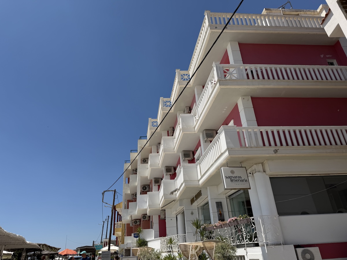 Weiße und rote Unterkunft mit Balkonen in Potos auf Thassos, nahe einem sonnigen Strand und der Küste
