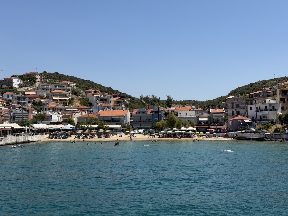 Türkises Wasser vor einer hellen Sandbucht mit Tavernen und Häusern am Hang bei Potos auf Thassos