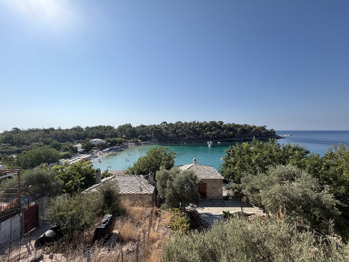 Blick auf Potos auf Thassos mit türkisblauer Bucht, Olivenbäumen und bewaldeter Küste unter klarem Himmel