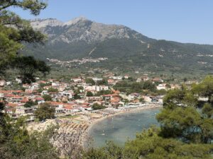Blick auf Potos auf Thassos mit dicht bebautem Küstenort, geschwungenem Strand und bewaldetem Bergpanorama im Süden