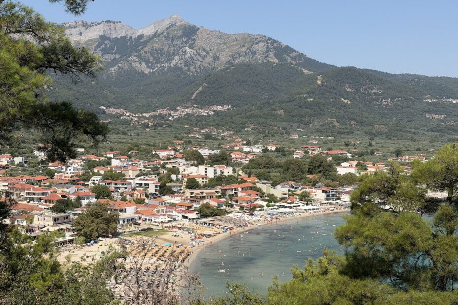 Blick aufSkala Potamias auf Thassos mit dicht bebautem Küstenort, geschwungenem Strand und bewaldetem Bergpanorama im Süden