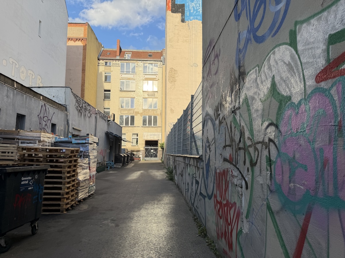 Ein enger Berliner Hinterhof mit bunten Graffitiwänden, Paletten und Altbau im Licht