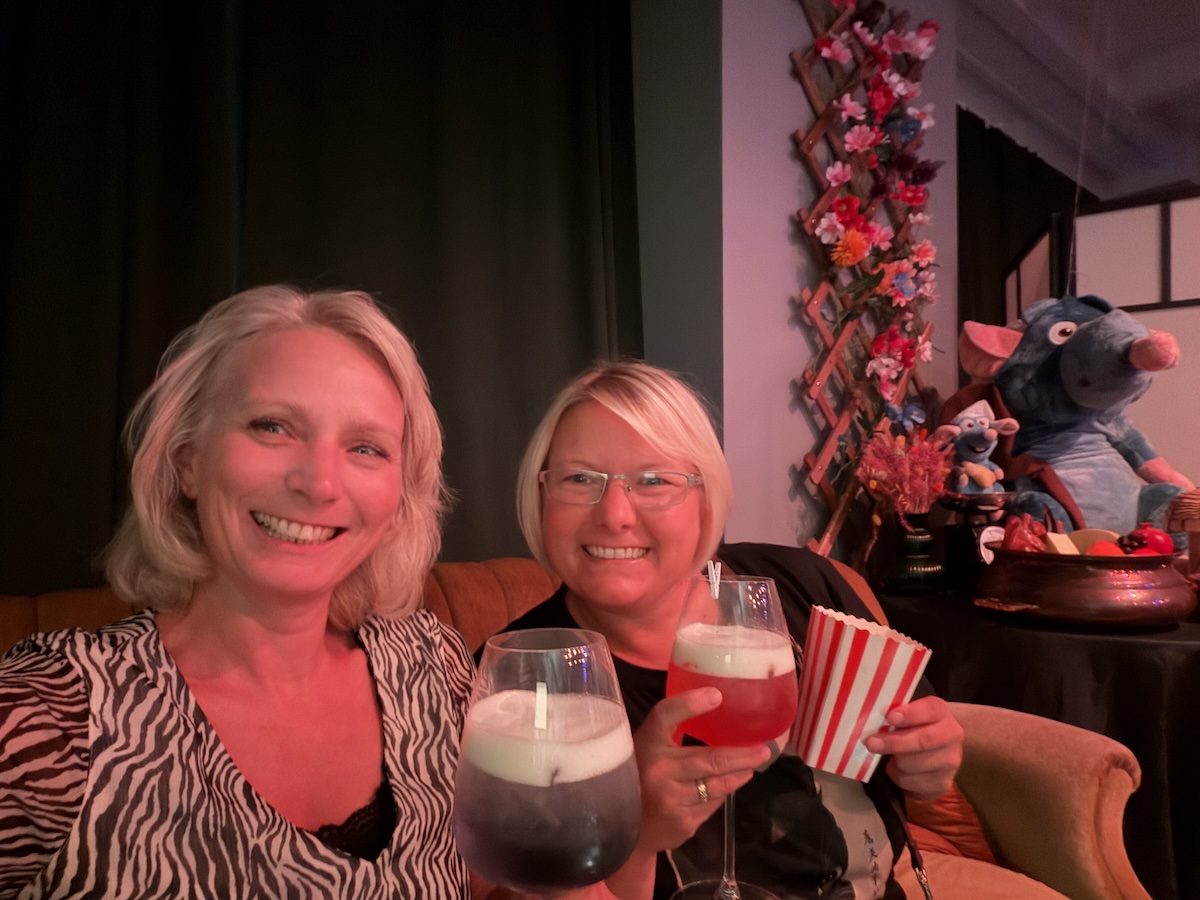 Zwei Frauen stoßen bei Movie2Menu Berlin mit Getränken an, während Ratatouille als Film und Dinner erlebt wird.