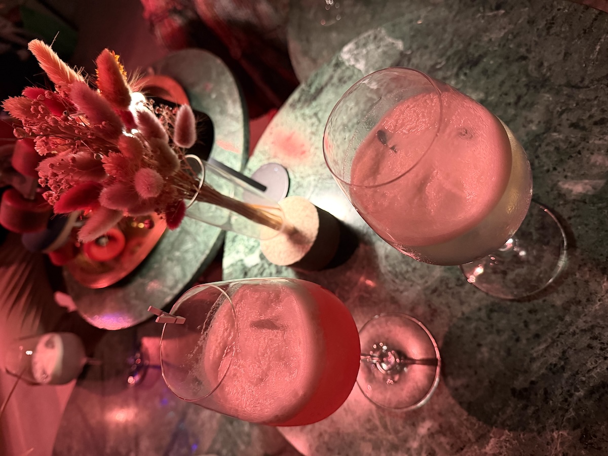 Zwei rosafarbene Drinks mit Eis stehen neben einer roten Blumendekoration Menu-Abend zu Ratatouille in Berlin.