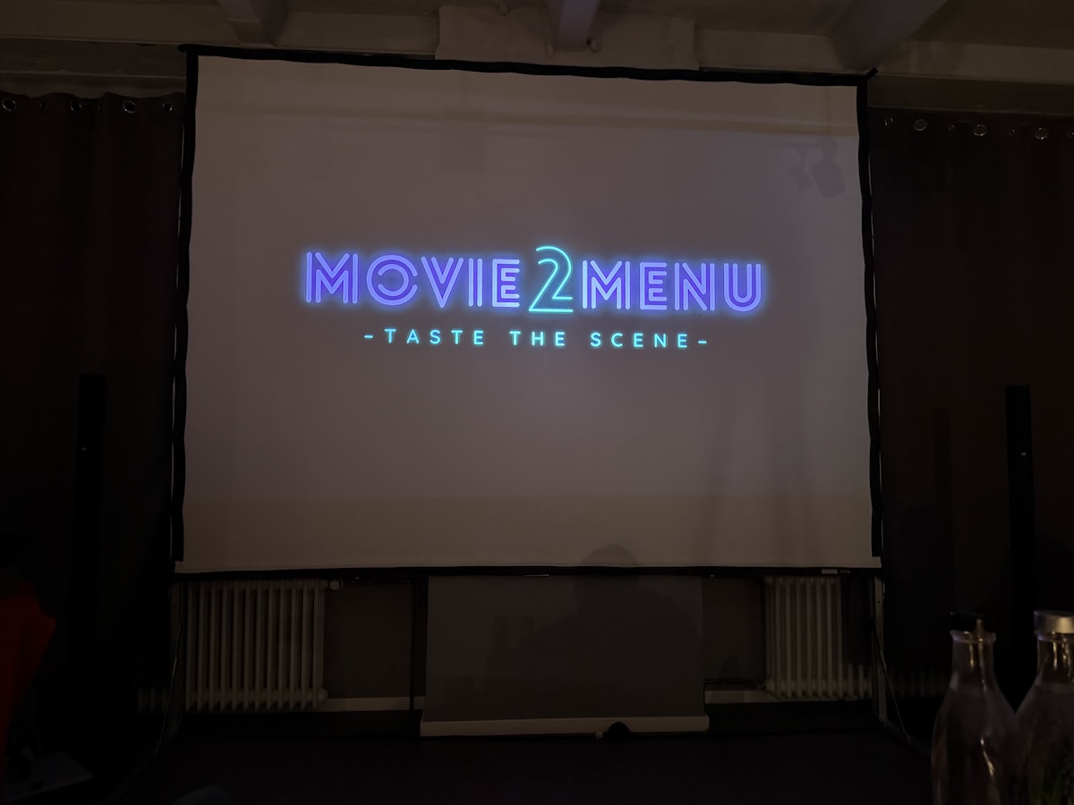 Leuchtendes Movie2Menu-Logo auf einer Leinwand beim Dinner zum Film in Berlin-Kreuzberg mit Ratatouille-Bezug