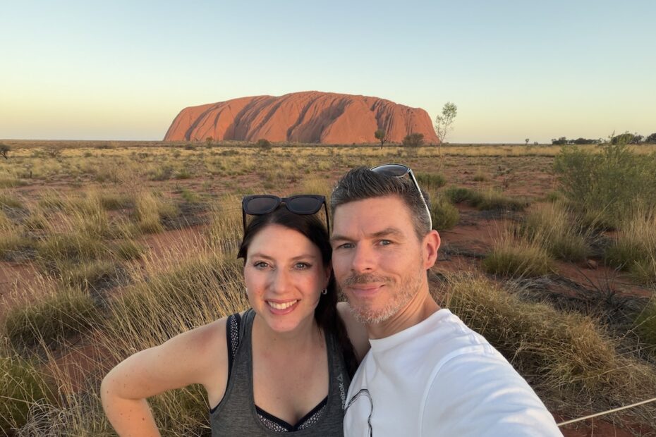 Florian und eine Frau posieren vor dem roten Uluru in trockener Landschaft als Reiseblogger-Porträt zum Business-Wachstum