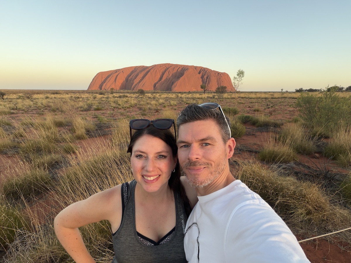Florian und eine Frau posieren vor dem roten Uluru in trockener Landschaft als Reiseblogger-Porträt zum Business-Wachstum