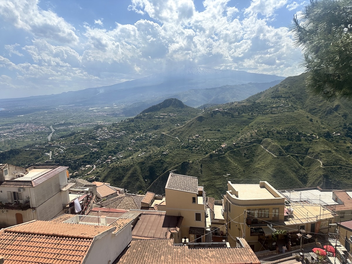 Über einem grünen Tal mit verstreuten Häusern liegen wolkenverhangene Berge und ein weiter Himmel.