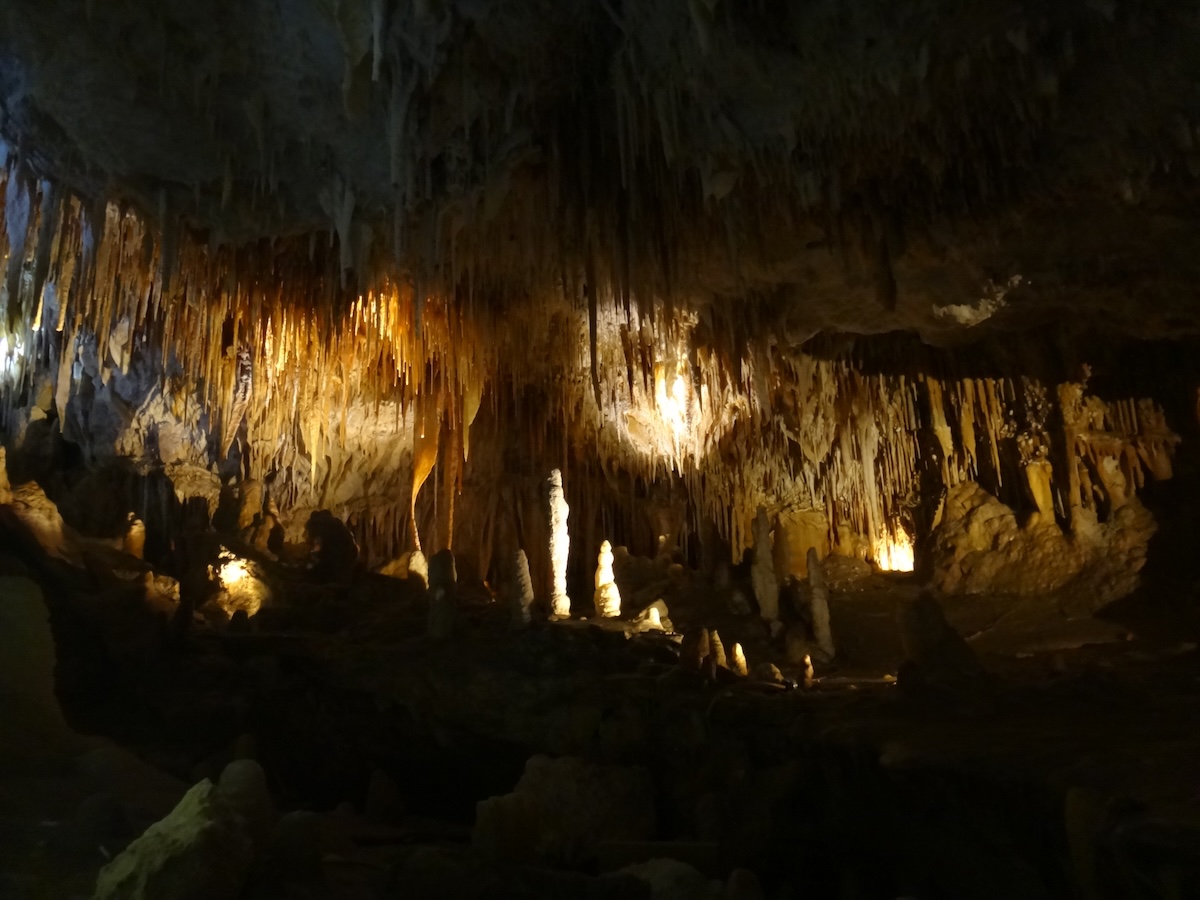 Goldene Beleuchtung lässt Stalaktiten und Stalagmiten in einer weitläufigen Tropfsteinhöhle sichtbar werden.