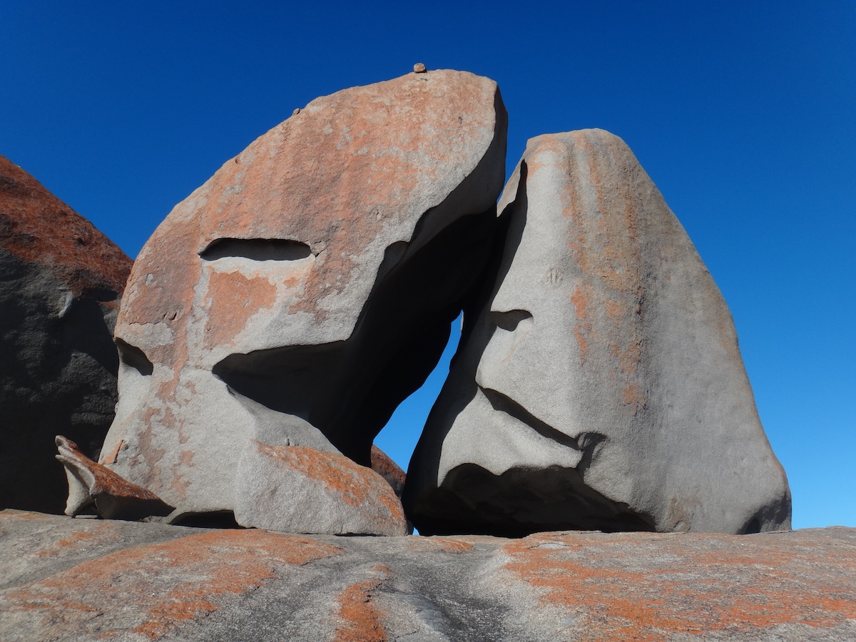 Rötlich verwitterte Granitfelsen bilden ein natürliches Felstor vor tiefblauem Himmel und zeigen markante, gerundete Formen.