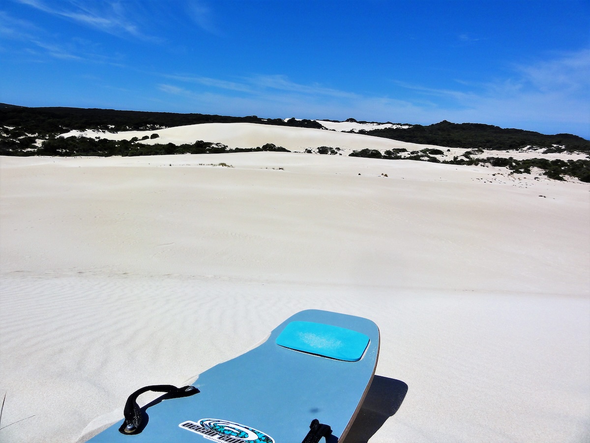 Ein blaues Sandboard liegt auf den weißen Dünen von Little Sahara auf Kangaroo Island unter klarem blauem Himmel.