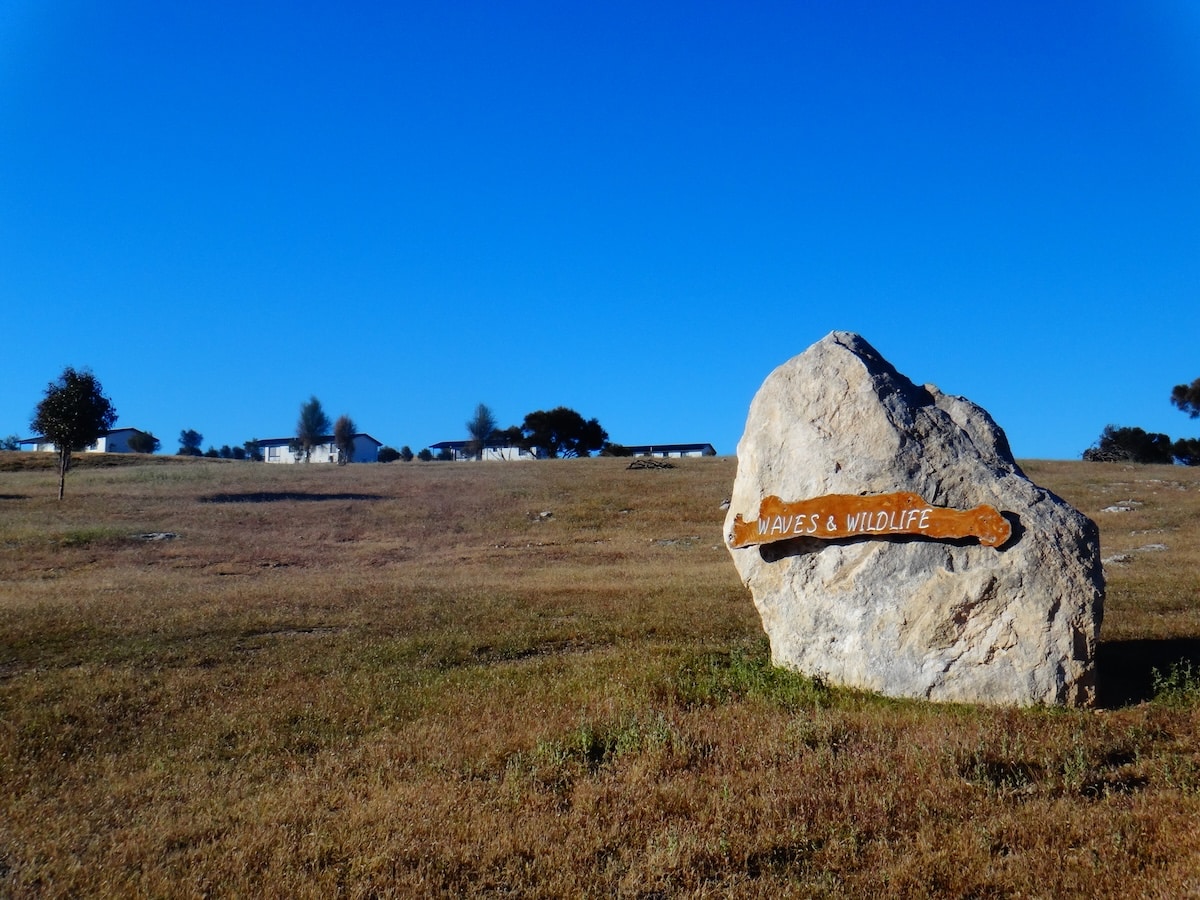 Ein hölzerner Wegweiser zu Waves & Wildlife steht auf einer offenen Landschaft bei Stokes Bay auf Kangaroo Island.