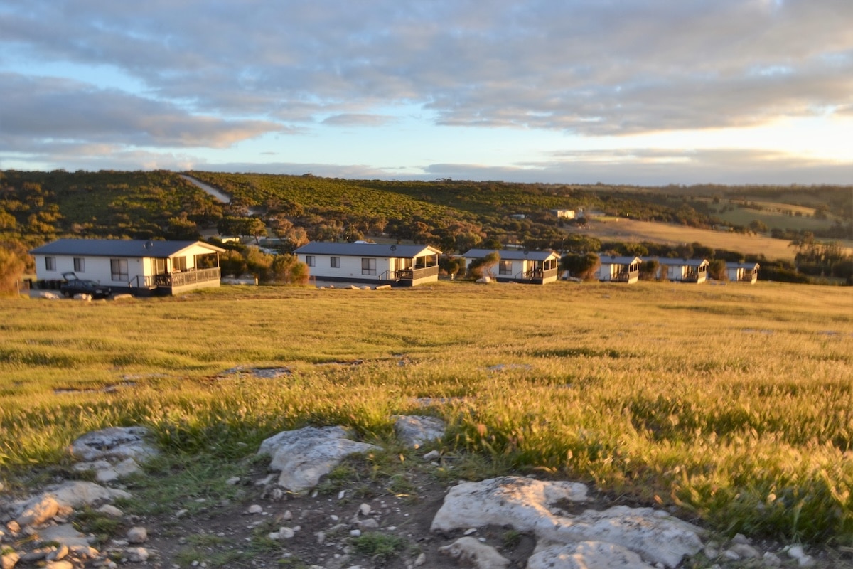 Mehrere Unterkünfte liegen in der weiten Landschaft von Stokes Bay auf Kangaroo Island bei warmem Abendlicht.