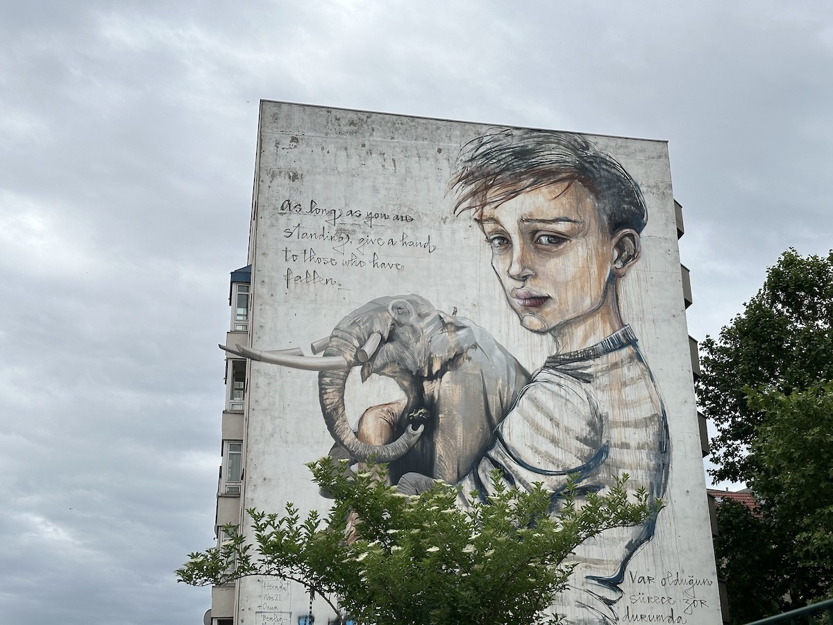 Ein großes Berliner Streetart-Wandbild zeigt ein Mädchen mit einem Elefanten vor einer grauen Hausfassade.