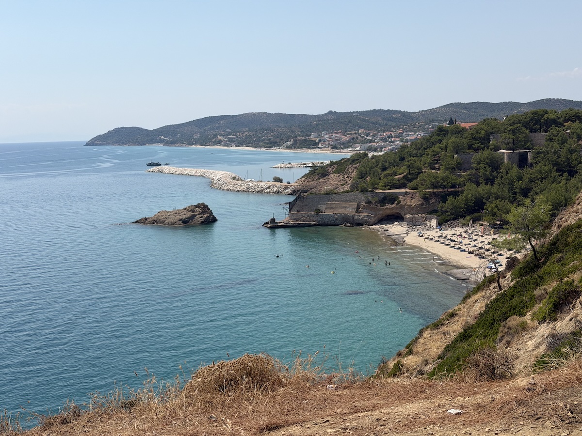 Eine geschützte Bucht auf Thassos mit türkisblauem Wasser, hellem Kiesstrand und bewaldeten Hügeln entlang der Küste.