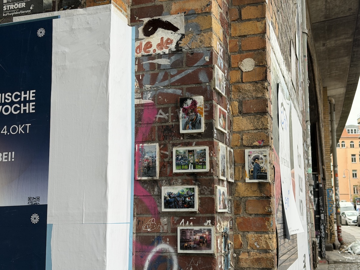 Mehrere gerahmte Streetart-Werke und Graffiti bedecken eine rotbraune Ziegelwand in Berlin nahe Haus Schwarzenberg.
