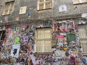 Bunte Streetart mit Murals, Paste-ups und Stickern bedeckt eine verwitterte Berliner Hausfassade nahe verschiedener Kieze.