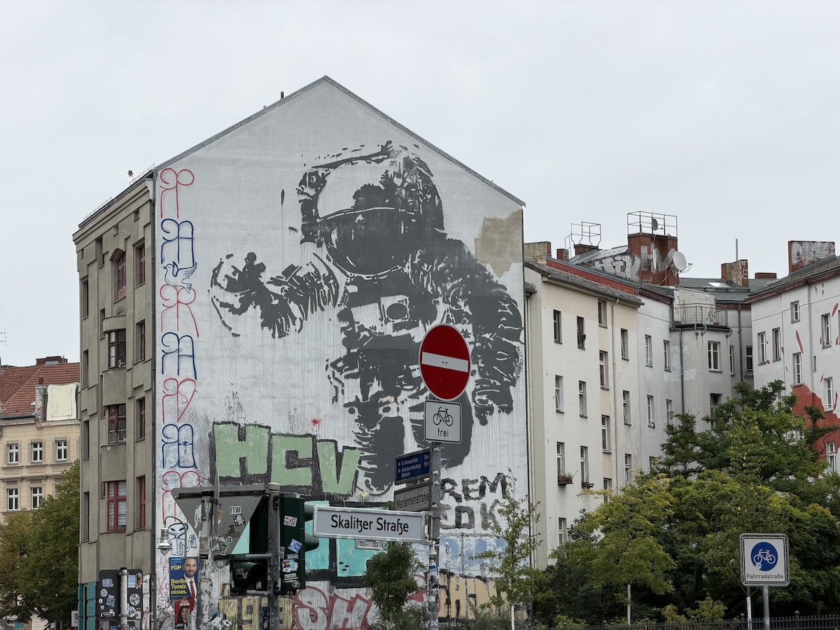 Großes Berliner Mural mit einer astronautischen Figur an einer Hausfassade und Graffiti im urbanen Stadtbild