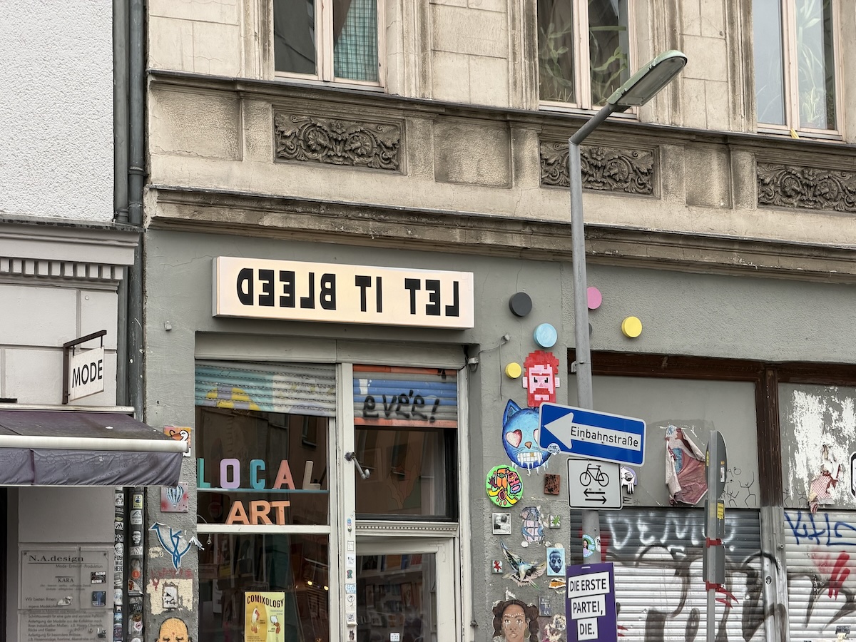 Bunte Streetart mit Stickern, Schildern und dem Schriftzug „LET IT BLEED“ an einer Berliner Hausfassade