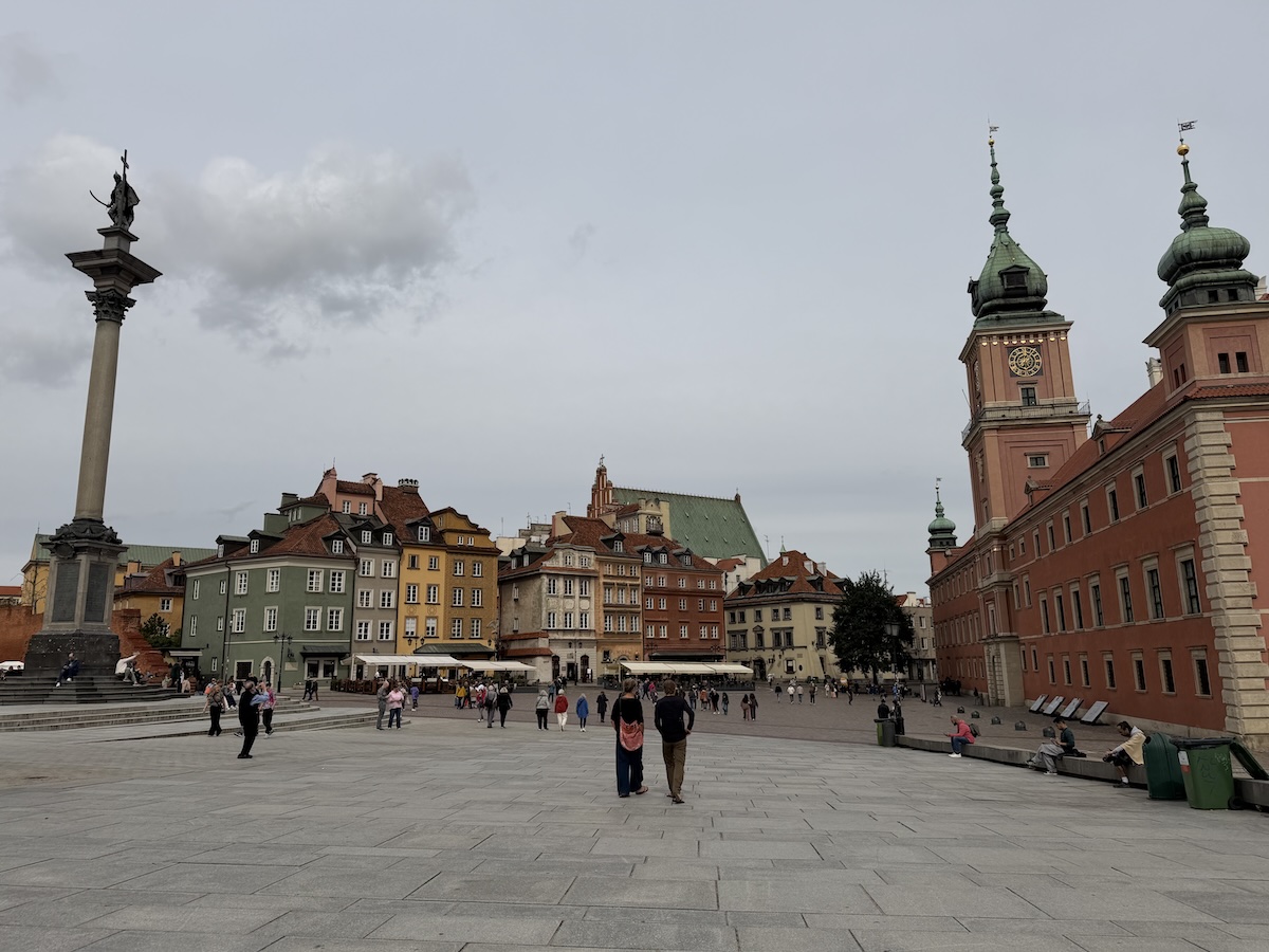 Der Schlossplatz in Warschau zeigt das Königsschloss, historische Häuser und die Sigismundsäule mit Besuchern.