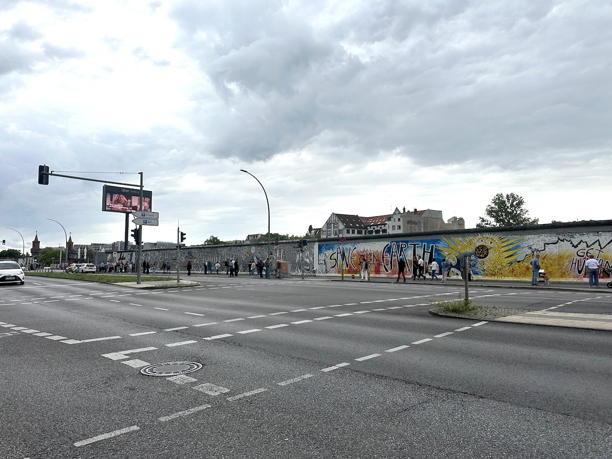 Bunte Streetart auf einem erhaltenen Abschnitt der Berliner Mauer an einer breiten Kreuzung in Berlin mit Radfahrern