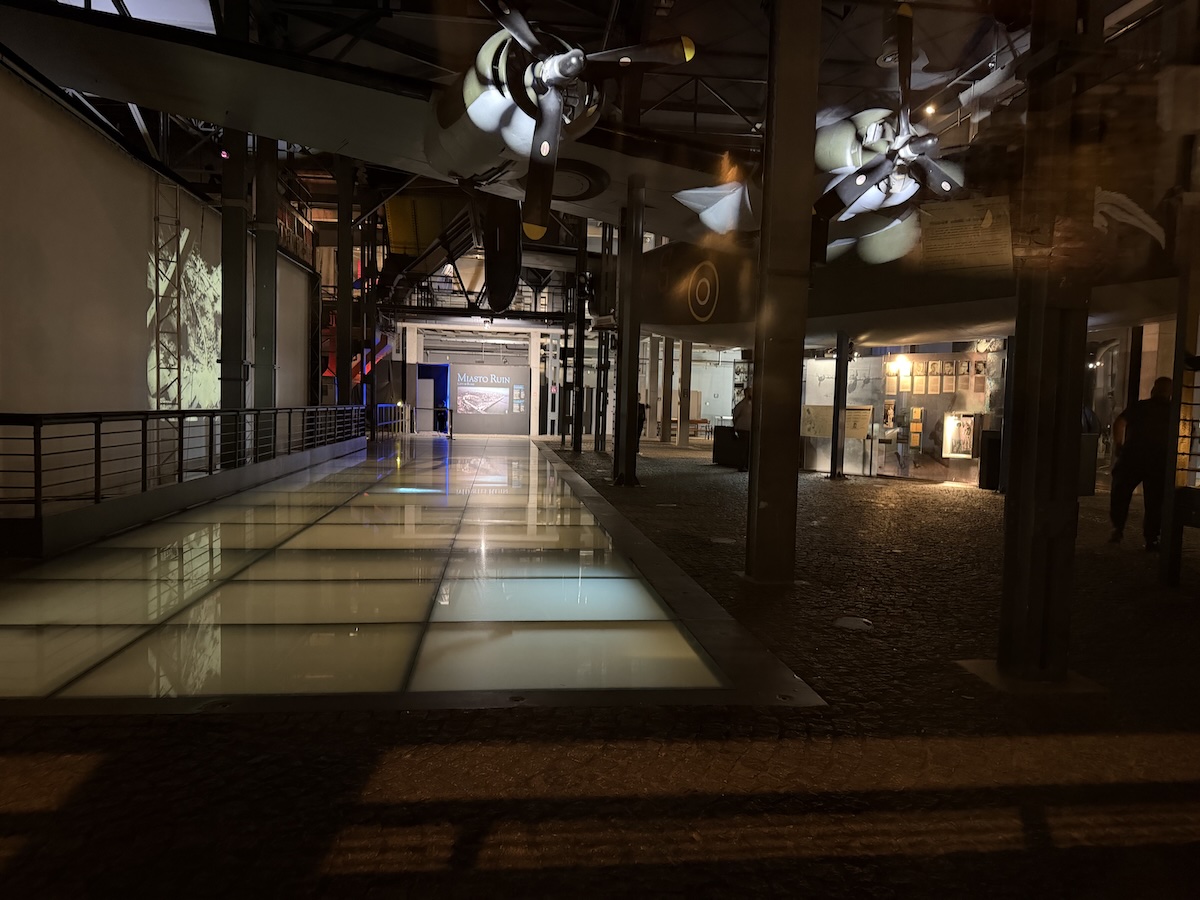 Dunkler Museumsbereich in Warschau mit historischen Flugzeugen, Glasboden und einer Ausstellung zur Stadtgeschichte.