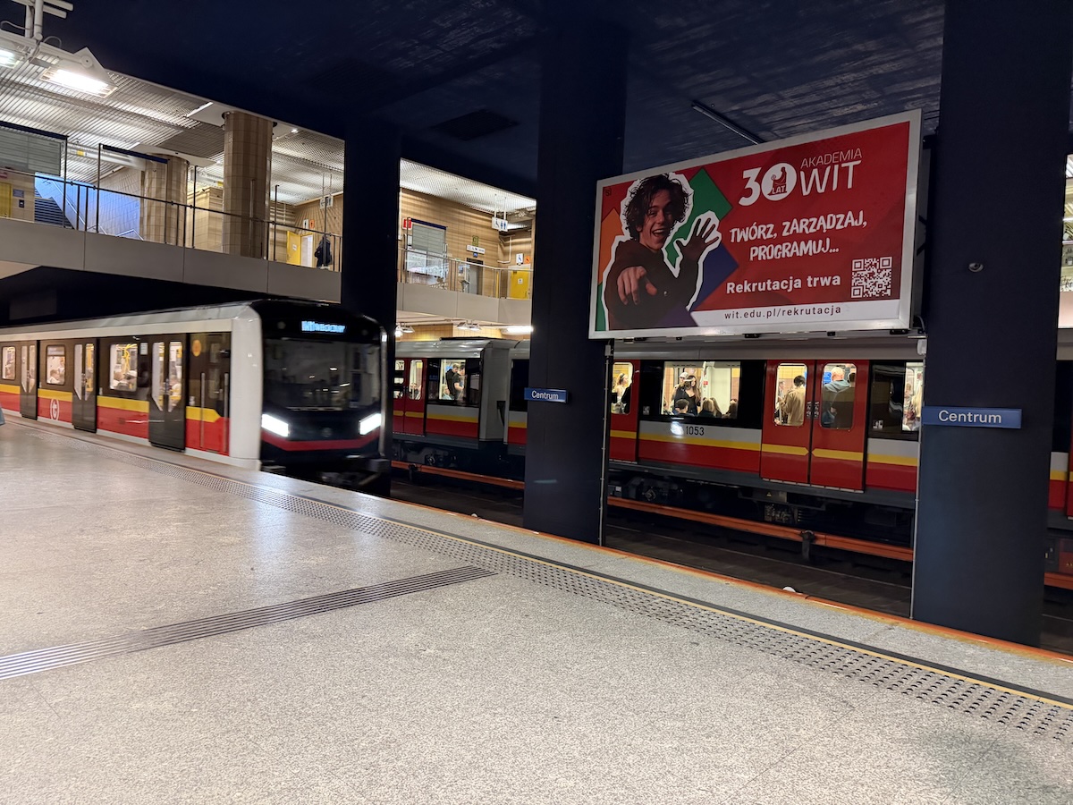 Rote und gelbe Metrozüge halten an der Station Centrum in Warschau unter einer unterirdischen Bahnsteighalle.