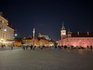 Beleuchteter Schlossplatz in Warschau mit Königsschloss, Sigismundsäule und historischen Häusern der Altstadt bei Nacht.