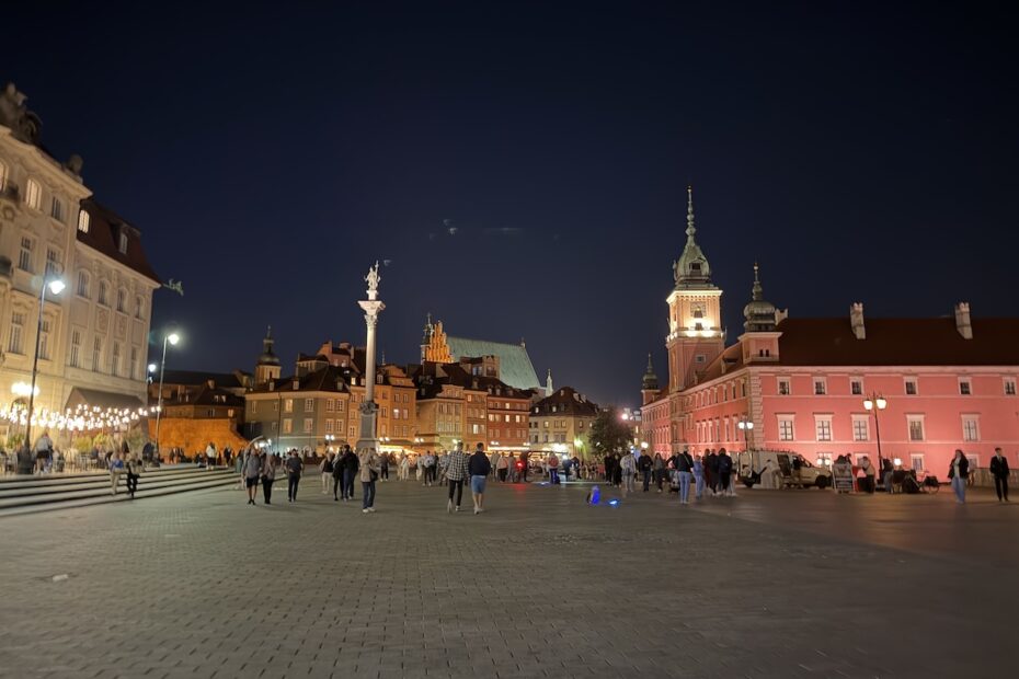 Beleuchteter Schlossplatz in Warschau mit Königsschloss, Sigismundsäule und historischen Häusern der Altstadt bei Nacht.