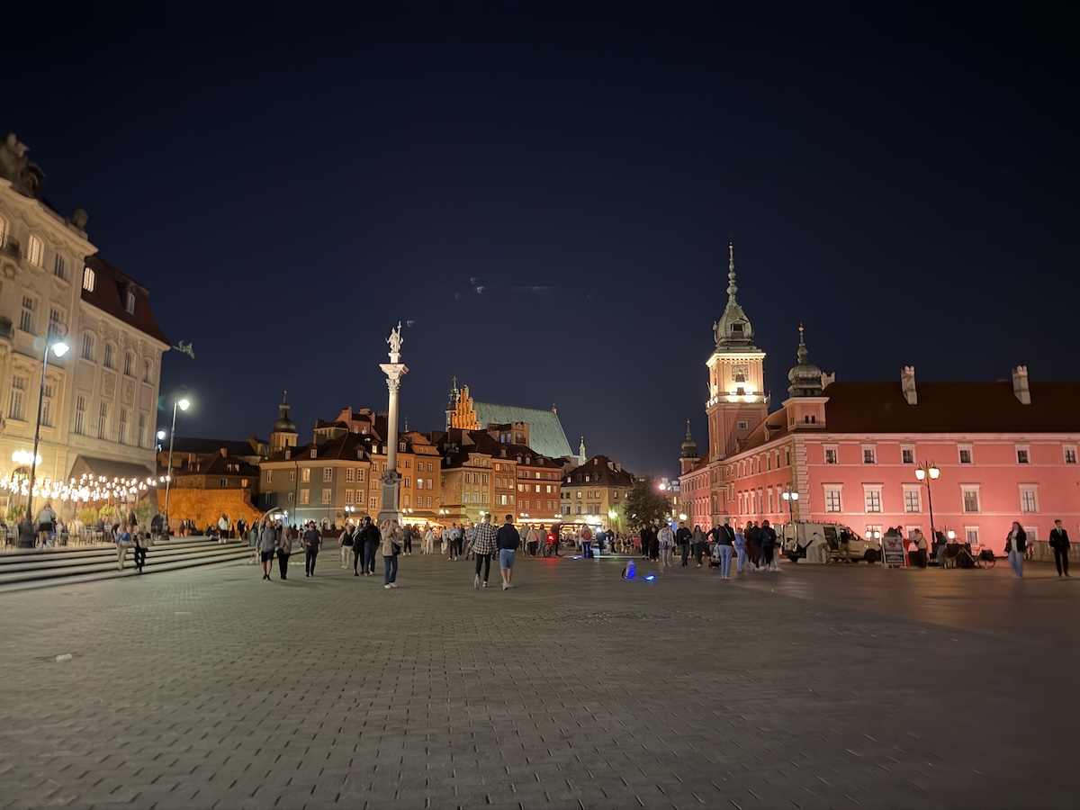 Beleuchteter Schlossplatz in Warschau mit Königsschloss, Sigismundsäule und historischen Häusern der Altstadt bei Nacht.