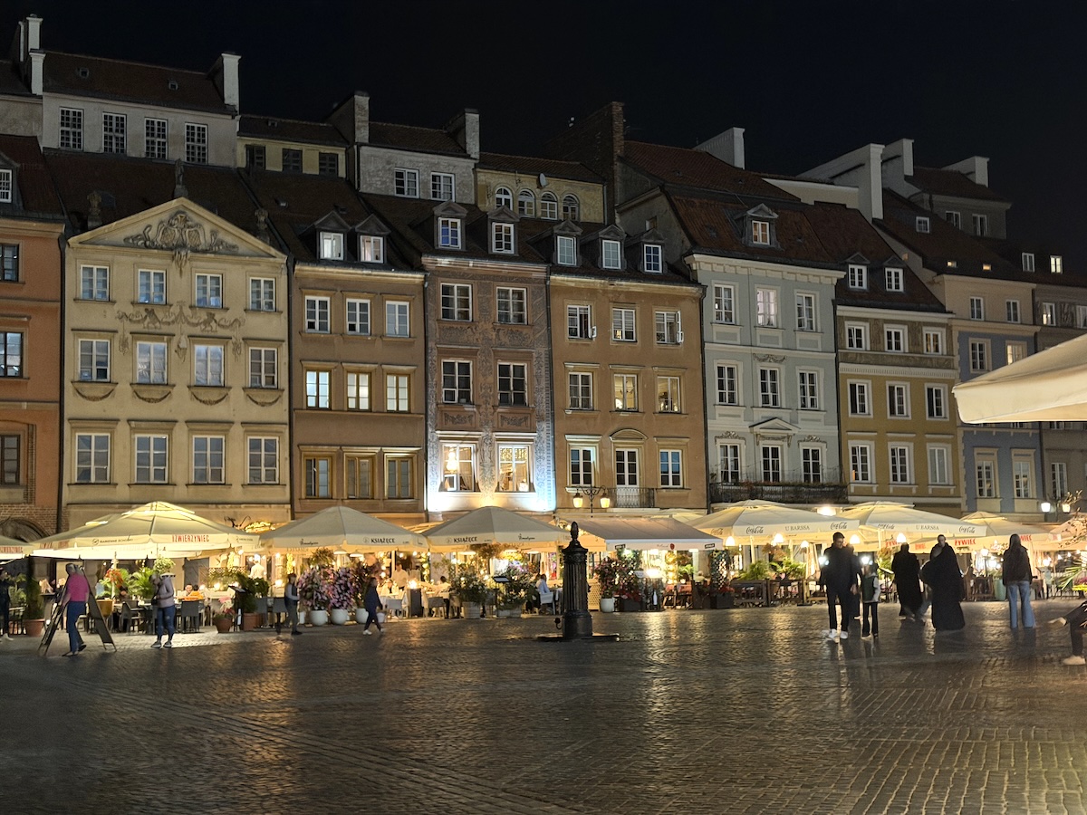 Historische Häuser am Altstadtmarkt in Warschau mit beleuchteten Cafés und Restaurants am Krakowskie Przedmieście bei Nacht.