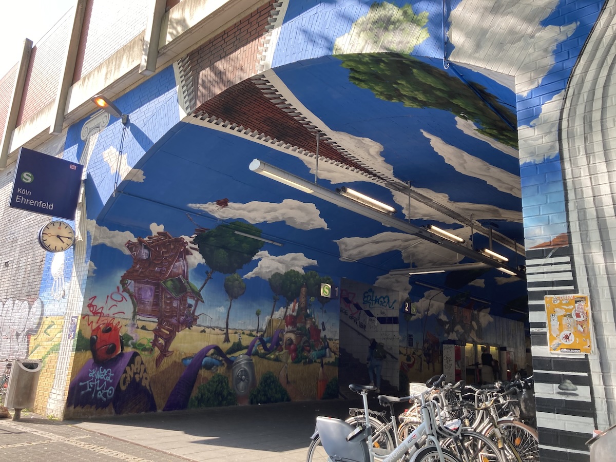 Farbenfrohes Streetart-Wandbild mit Fantasieszene unter einer Brücke in Köln-Ehrenfeld neben abgestellten Fahrrädern