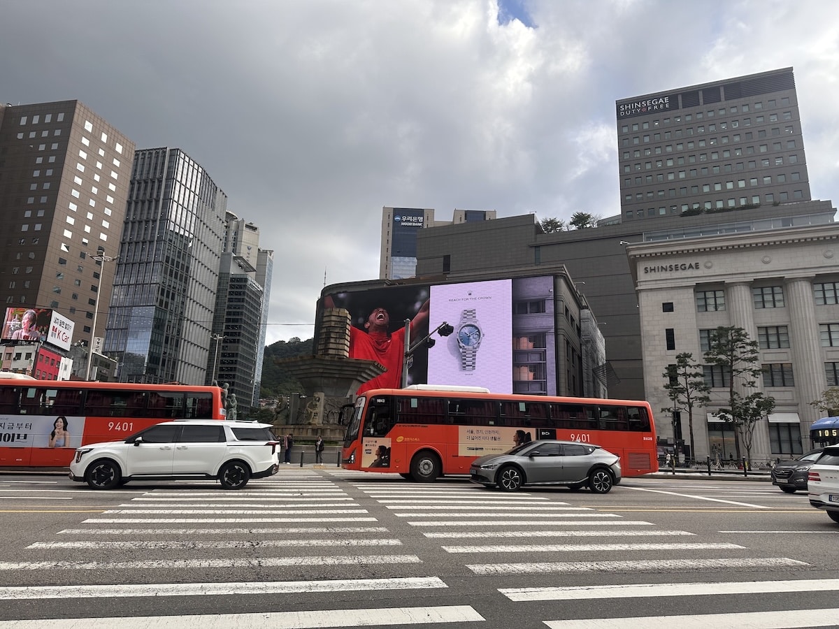 Rote Stadtbusse fahren an einer belebten Kreuzung in Seoul vor Hochhäusern