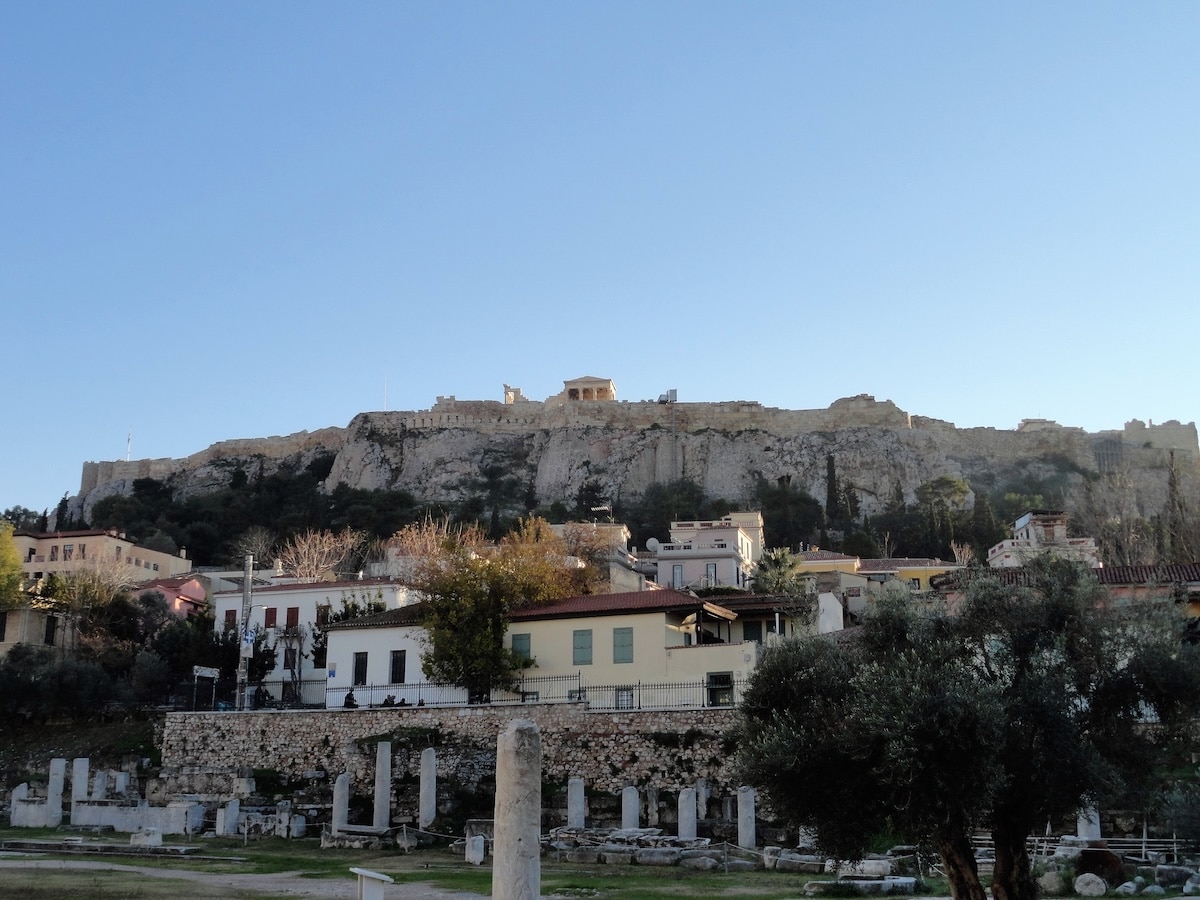 Über antiken Ruinen und Wohnhäusern erhebt sich die Akropolis von Athen auf ihrem felsigen Hügel im klaren Tageslicht.